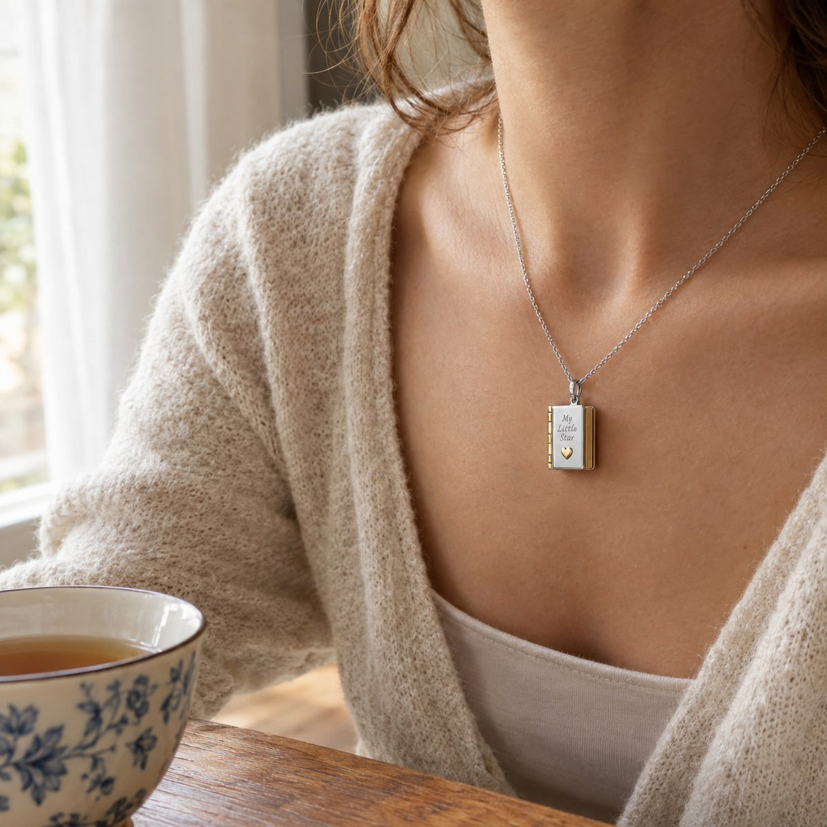 A woman at a table wearing the Pomence My Little Star Book Locket Necklace, the pendant at her collarbone