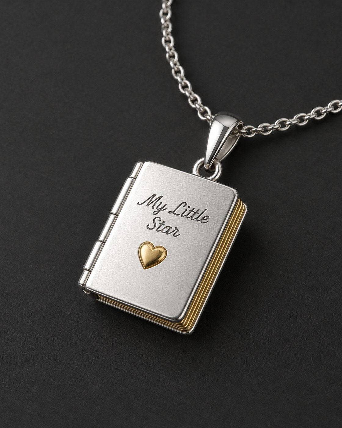 The Pomence My Little Star Book Locket Necklace and its chain on a dark charcoal background