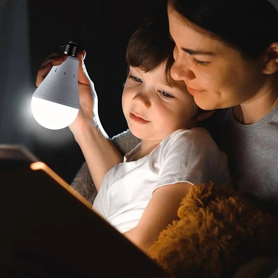 A mother and her son reading together by the light of the rechargeable bulb in a dark room