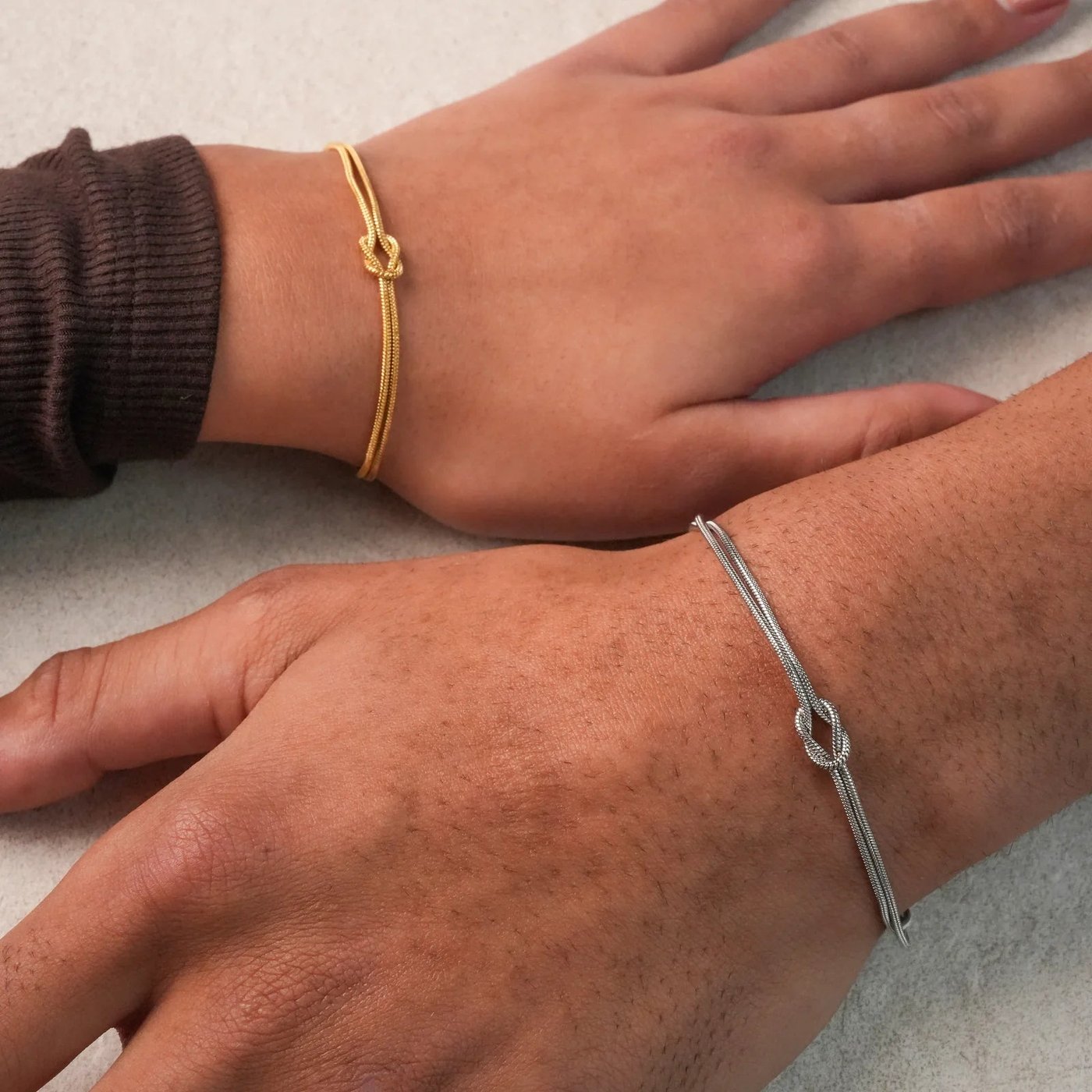 The warm 18k-gold tone and the cool steel-silver tone of the Pomence Forever Knot Bracelet side by side