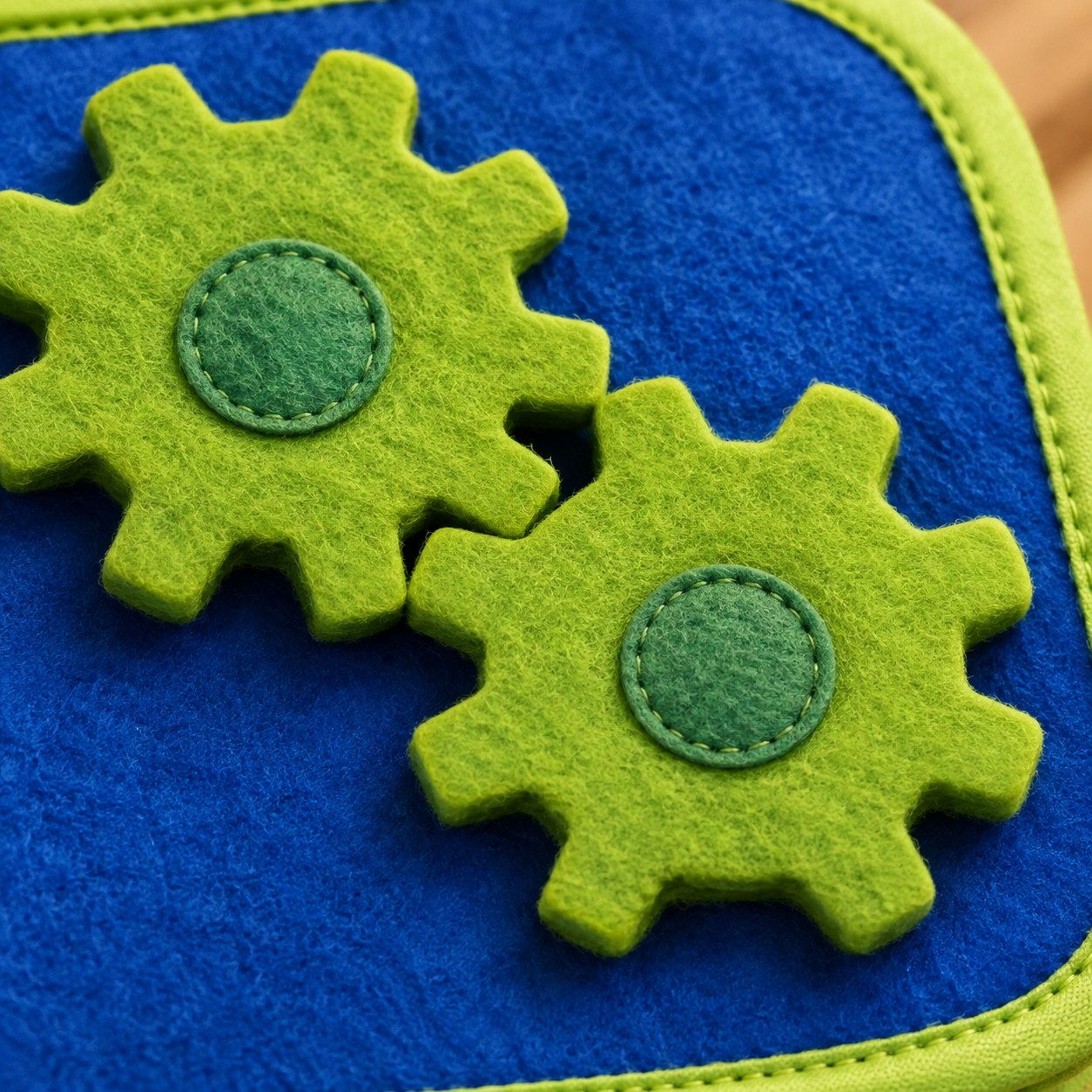 Close-up of two bright green felt turning gears interlocked on the Pomence Montessori Busy Board