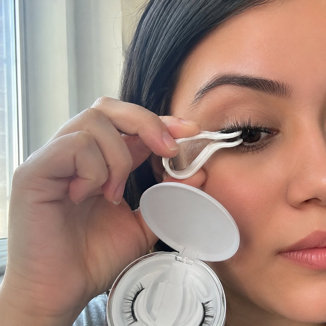 Hand using the Pomence spring-clip applicator to apply a magnetic lash