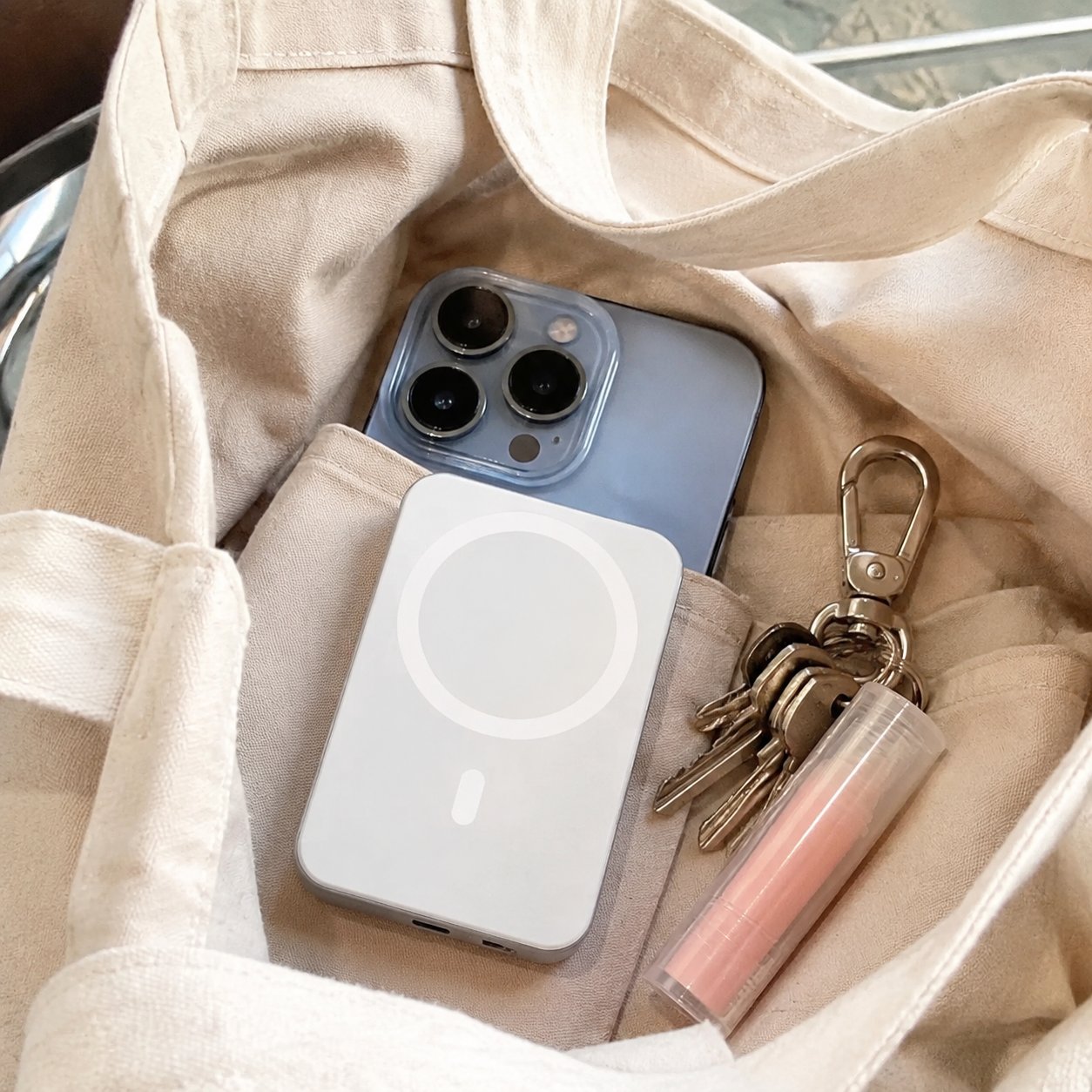 Compact Pomence power bank next to a phone in a tote bag