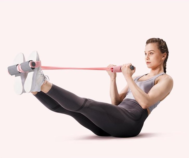 A woman in a V-sit pulling the Pomence Pedal Resistance Band toward her chest with her feet in the pedals