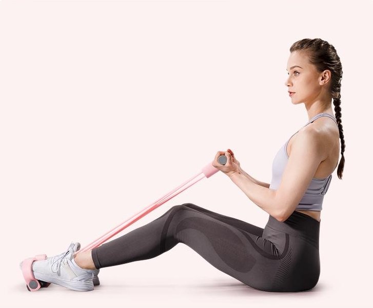 A woman sitting with her feet in the pedals doing a seated row with the Pomence Pedal Resistance Band