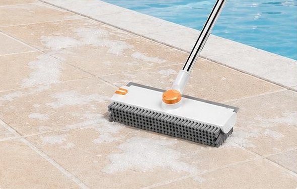 The brush scrubbing a soapy stone floor next to a pool