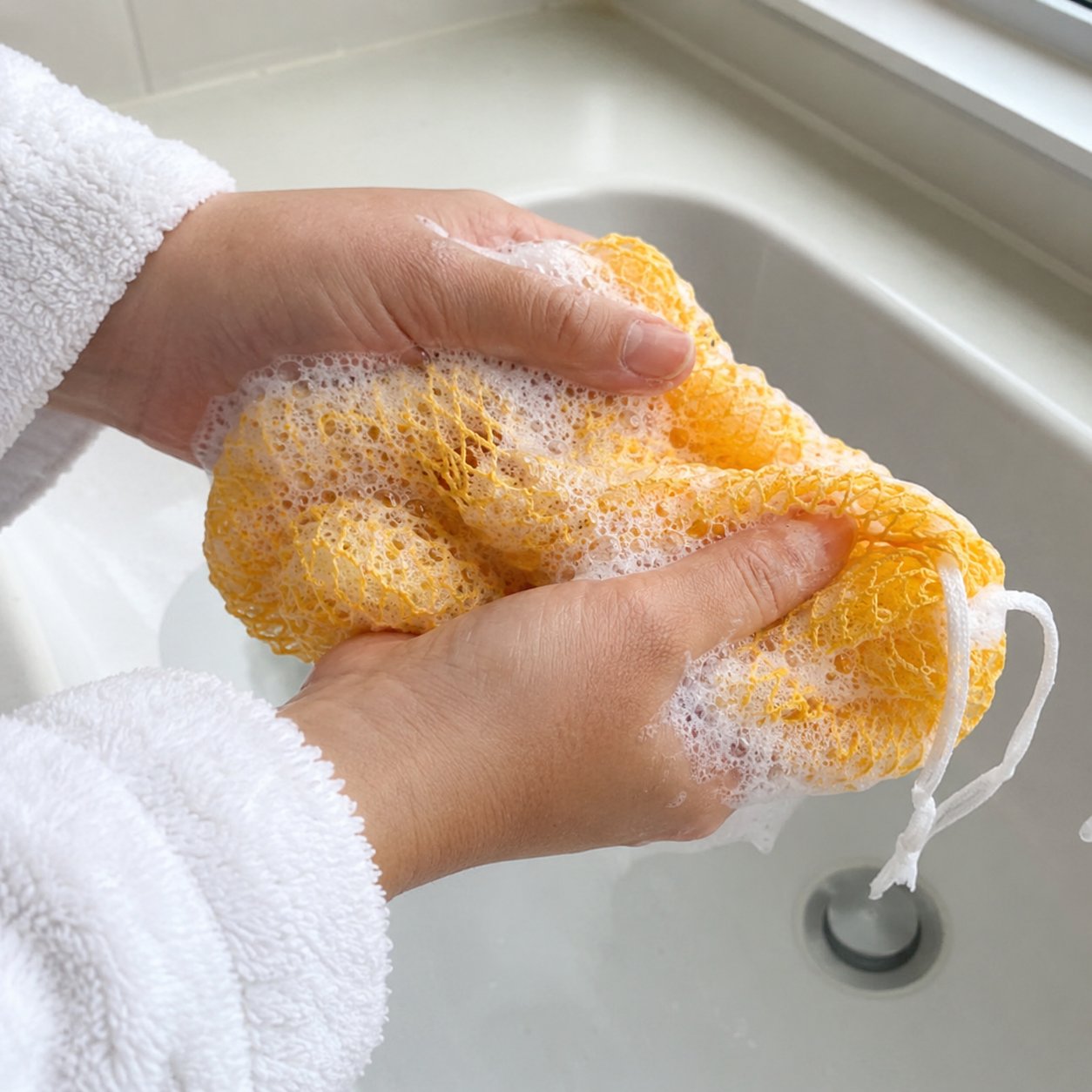 Hands squeezing the yellow net sponge full of body-wash foam