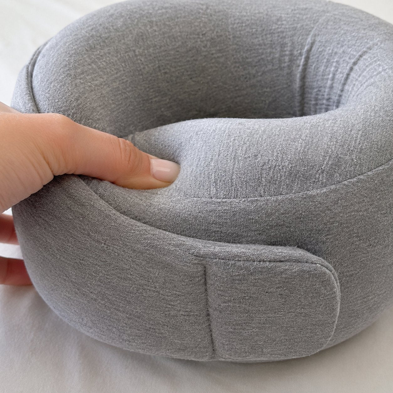 Fingers pressing into the memory foam of the Pomence Wrap Travel Neck Pillow, showing it spring back