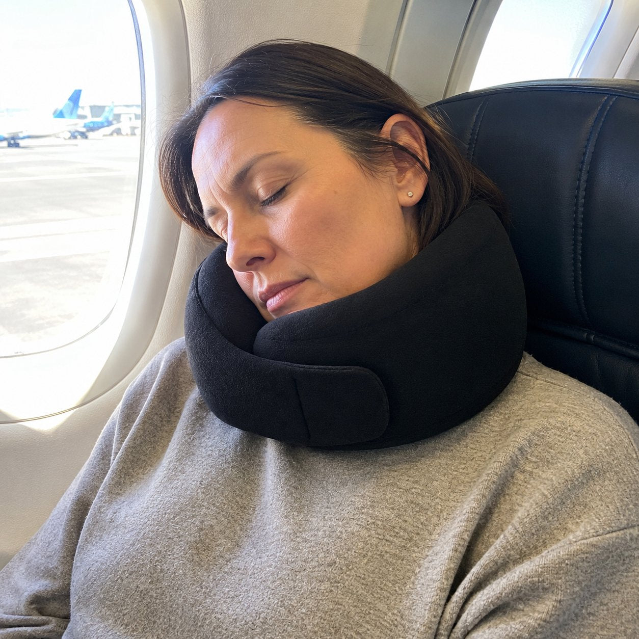 Woman asleep in an airplane seat wearing the Pomence Wrap Travel Neck Pillow