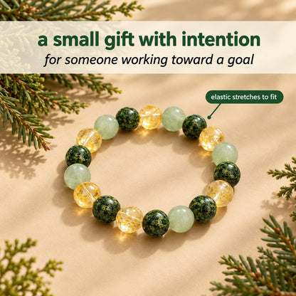 The Pomence Three Stone Abundance Bracelet staged on warm beige with evergreen sprigs