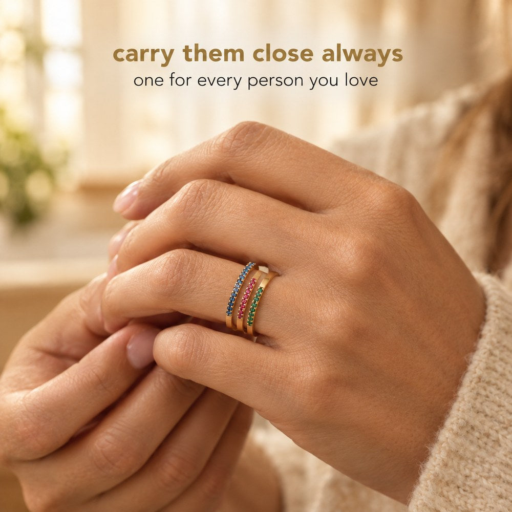 A hand wearing three Pomence Birthstone Stacking Rings in different birth month colors on one finger