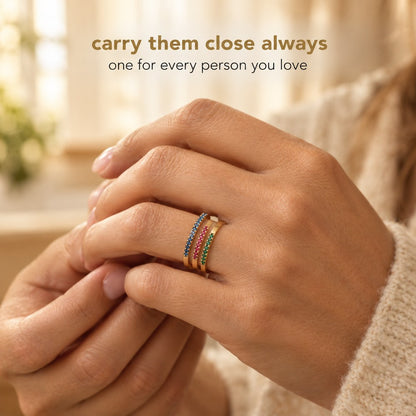 A hand wearing three Pomence Birthstone Stacking Rings in different birth month colors on one finger