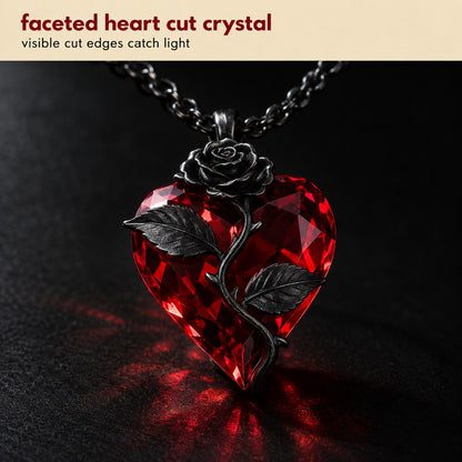 Macro of the Pomence Blood Rose Necklace pendant, the faceted blood red crystal heart with its cut edges, the sculpted gunmetal rose and the thorned stem with two leaves