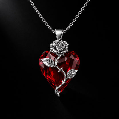 The Pomence Blood Rose Necklace in Silver, alone on a near black background, faceted red crystal heart with a bright silver rose and thorned stem