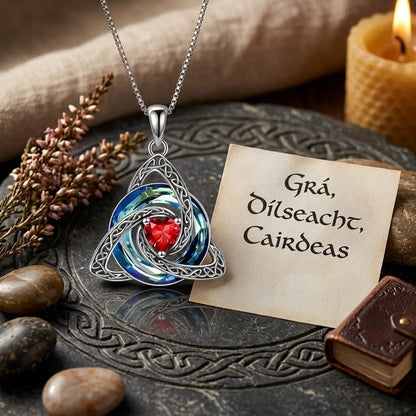 The Pomence Birthstone Celtic Knot Necklace laid on carved slate with heather and a Gaelic card