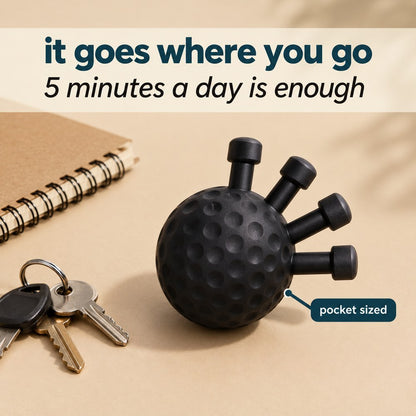 The matte black Pomence Forearm Grip Trainer Ball on a desk beside a notebook and a set of keys