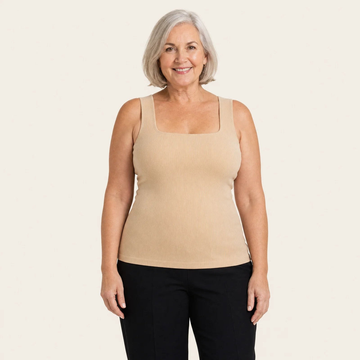 A smiling woman wearing the Pomence Front-Support Bra Tank in Beige with black pants