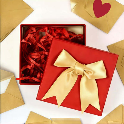 The red Pomence Love Notes Gift Box with its gold satin bow, red shredded filler and kraft envelopes