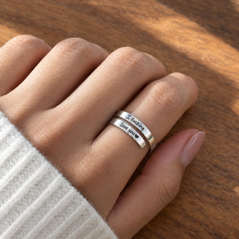 The Pomence I F♡cking Love You Ring worn on an adult hand resting on a wooden table