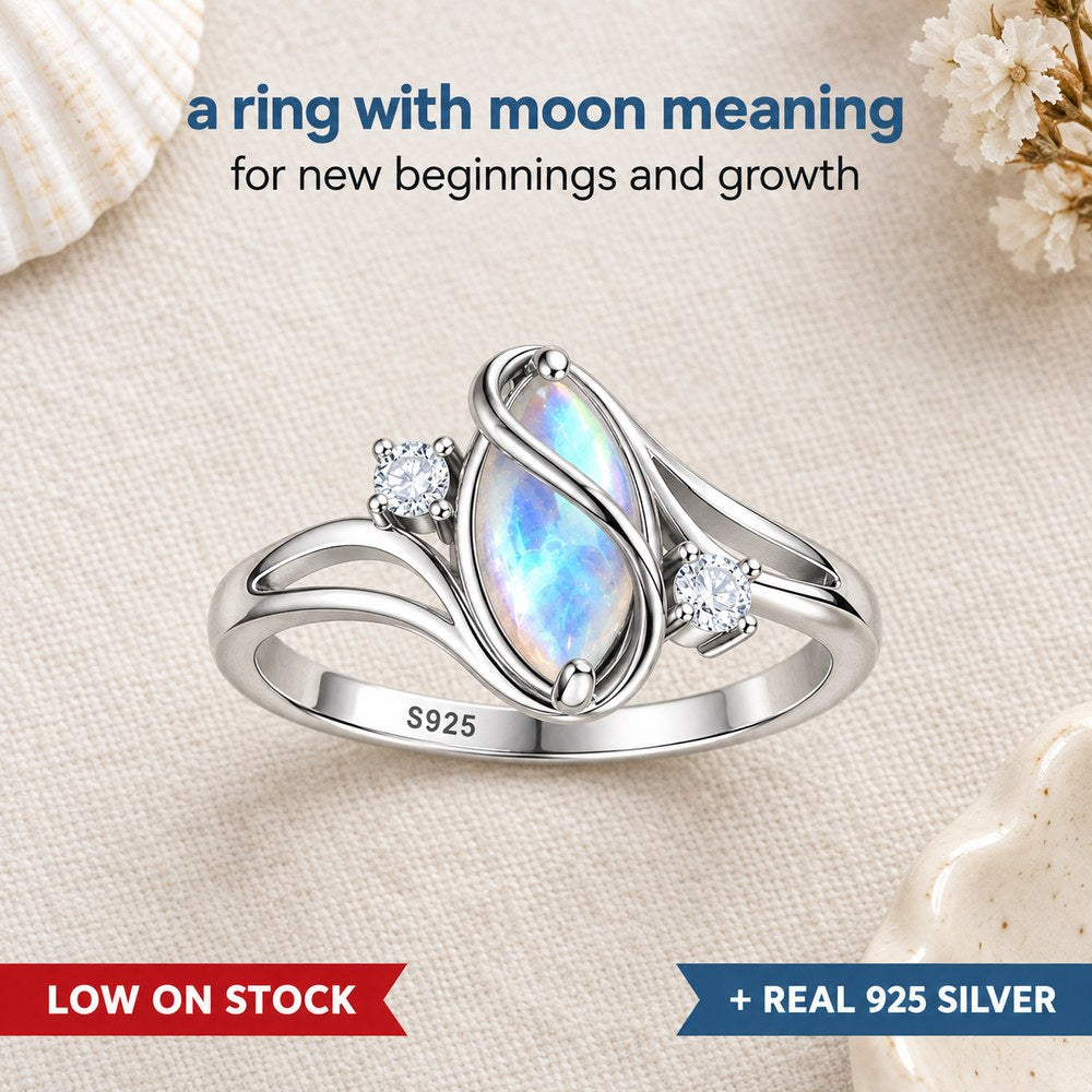 Flat lay of the Pomence Moonstone Ring on pale linen, the marquise moonstone flashing blue between two crossing silver ribbons