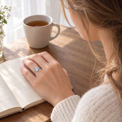 A woman at a table with an open journal and a cup of tea, wearing the Pomence Moonstone Ring