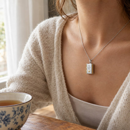 A woman at a table wearing the Pomence My Little Star Book Locket Necklace, the pendant at her collarbone