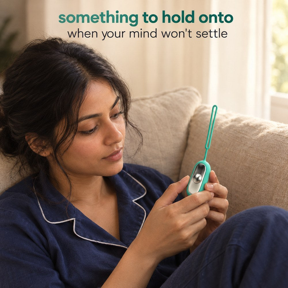 A woman on a sofa holding the Teal Palm Calm Fidget with her thumb on the domed metal button