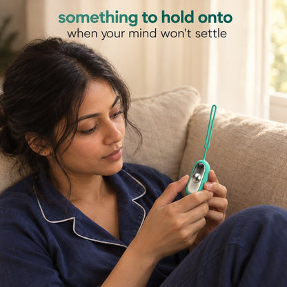 A woman on a sofa holding the Teal Palm Calm Fidget with her thumb on the domed metal button