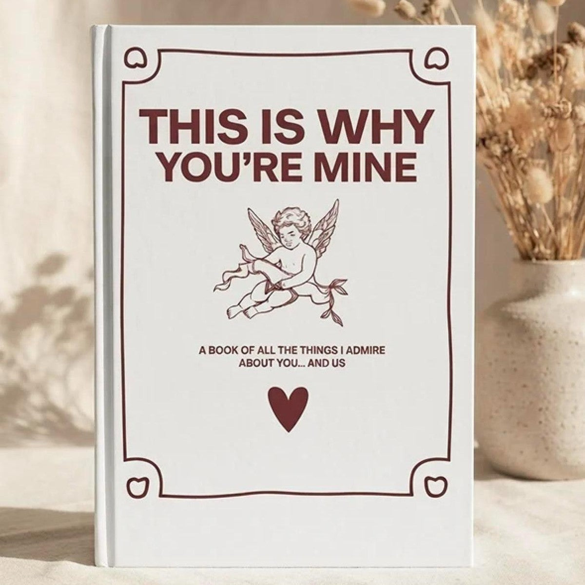 The Pomence couples guided journal standing on a table, white cover with a cupid drawing and a red heart