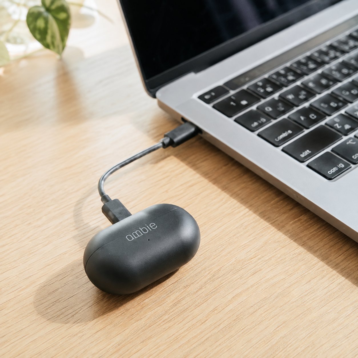 Ambie case charging on a USB-C cable next to a laptop