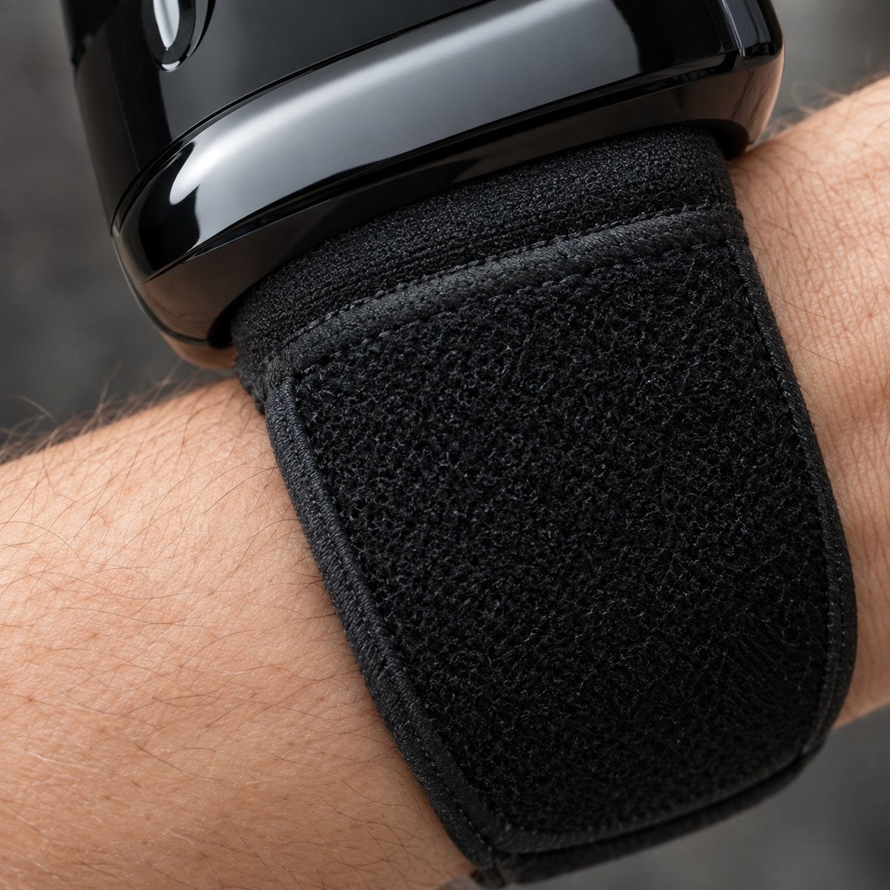 Macro of the black adjustable fabric band of the Pomence wrist blood pressure monitor fastened around an adult wrist