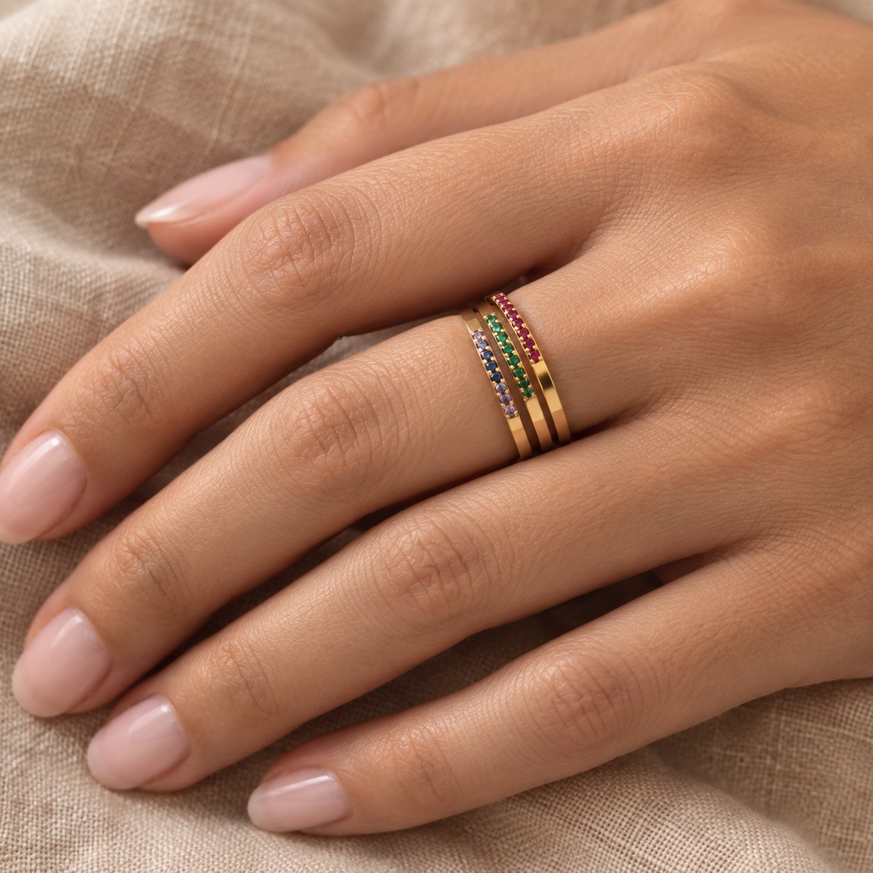 A hand wearing four thin gold tone Pomence Birthstone Stacking Ring bands stacked on one finger