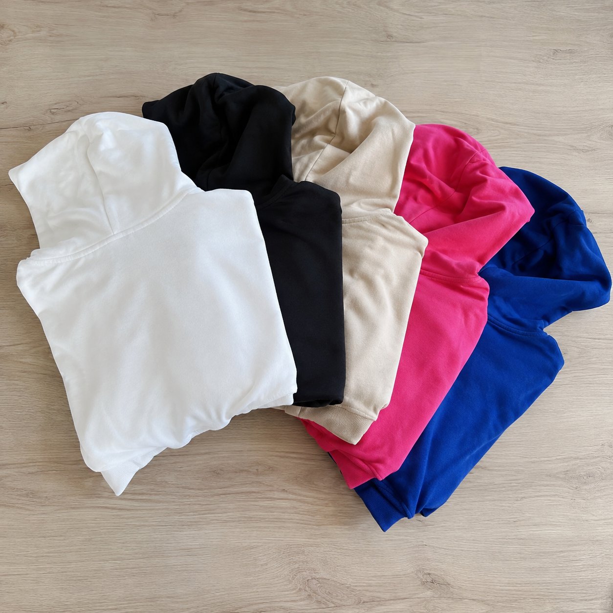 Five folded sweatshirts in white, black, beige, pink and blue