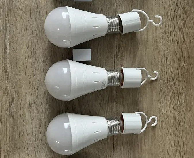 Three rechargeable bulbs laid out on a wood floor with their hook covers screwed on