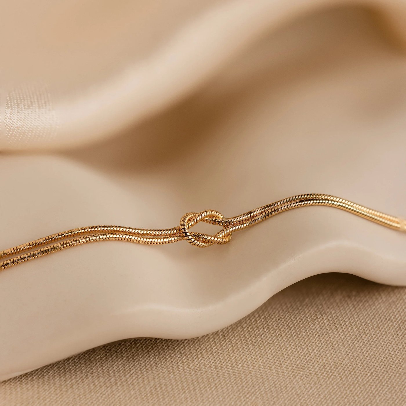 Macro of the single flat love knot on the Pomence Forever Knot Bracelet in warm 18k-gold tone with the eye of the knot open