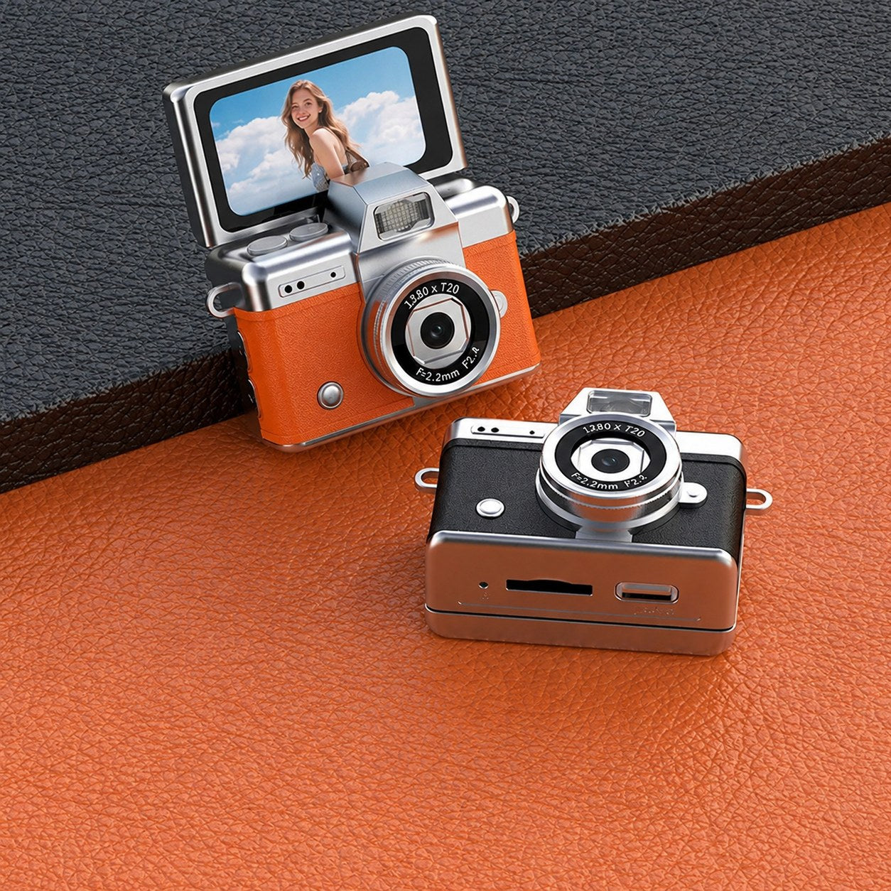 Two Pomence Mini Keychain Cameras in orange and black on a leather surface