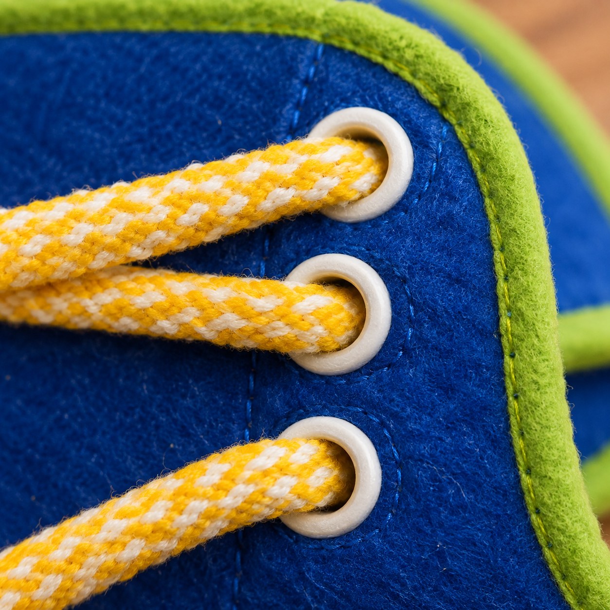 Close-up of a shoelace threaded halfway through the eyelets of a yellow and white felt shoe on the Pomence Montessori Busy Board