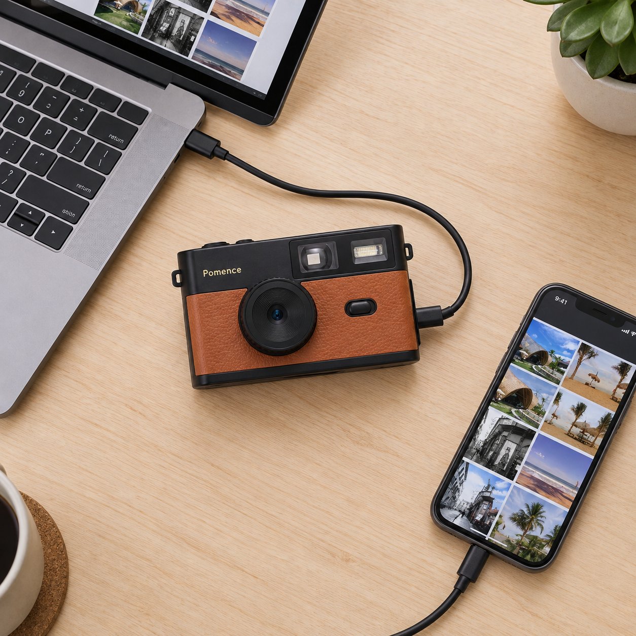 A hand holding the Pomence Mini Retro Camera on a desk with a USB-C cable plugged into its side, leading to a laptop