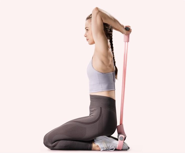 A woman kneeling on the pedals and pulling the handles up behind her head