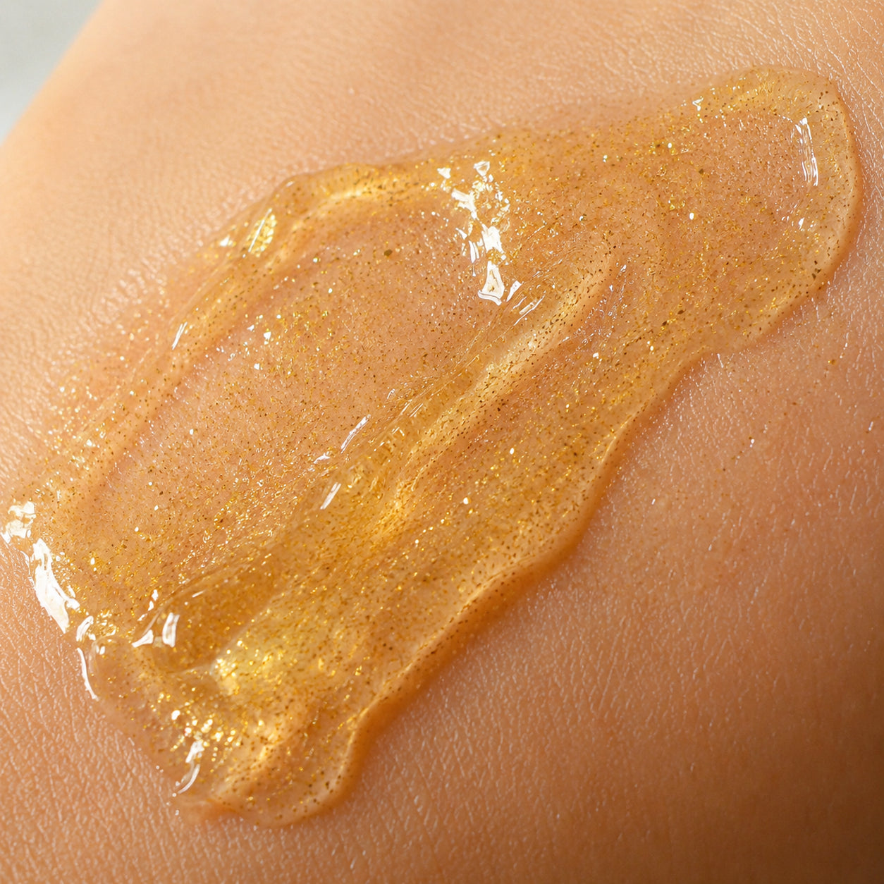 Close-up of gold-shimmer firming gel texture on smooth skin