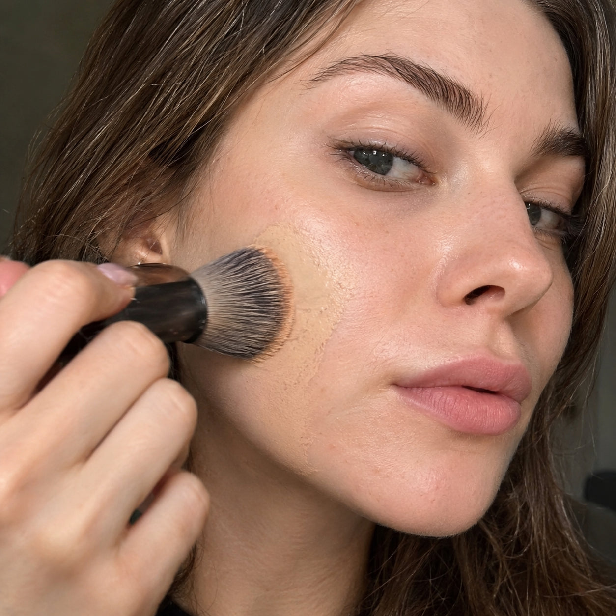 Woman blending foundation into her cheek with a makeup brush