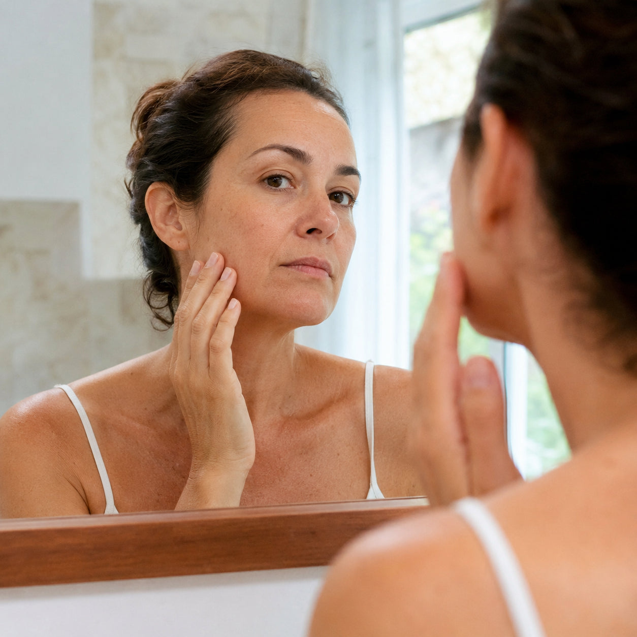 Woman checking her skin tone in a bright bathroom mirror before using Pomence Color Changing Foundation