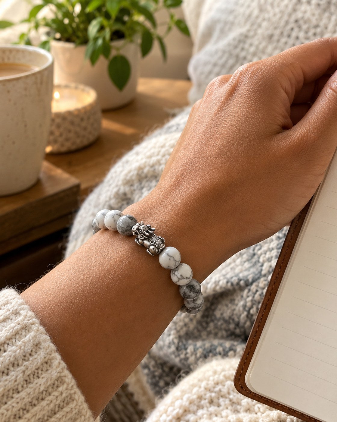 A woman's wrist wearing the Pomence Pixiu Wealth Bracelet, holding a journal in a reading nook in soft morning light