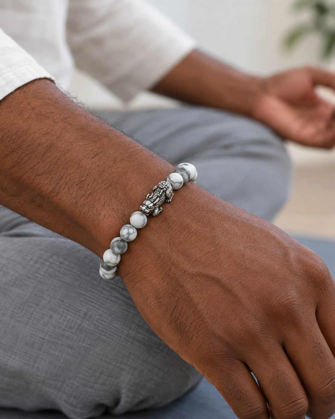 A man's wrist wearing the Pomence Pixiu Wealth Bracelet, hand resting in a meditative position on his knee
