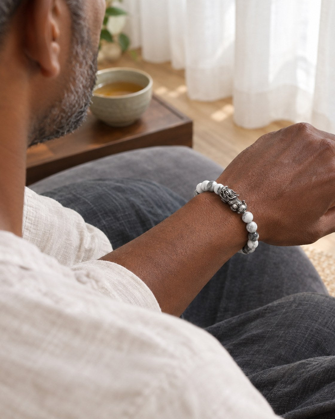 A man seated at a meditation cushion wearing the Pomence Pixiu Wealth Bracelet with the Pixiu charm visible on the top of his wrist