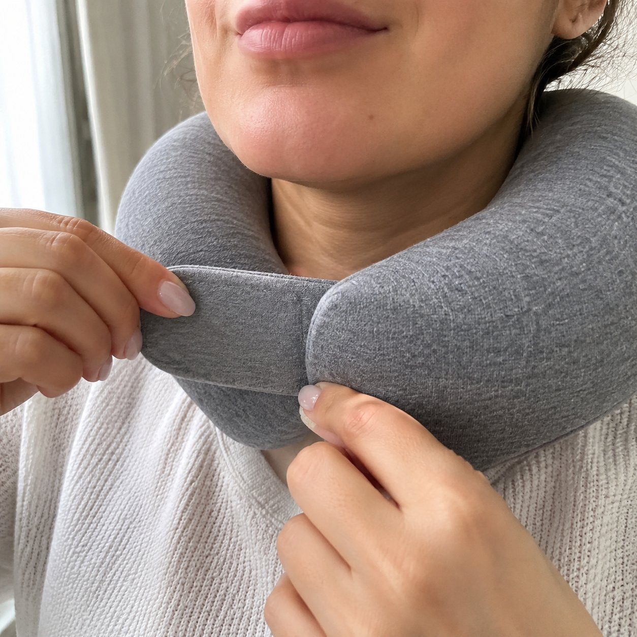 Hands adjusting the strap of the Pomence Wrap Travel Neck Pillow while it is worn
