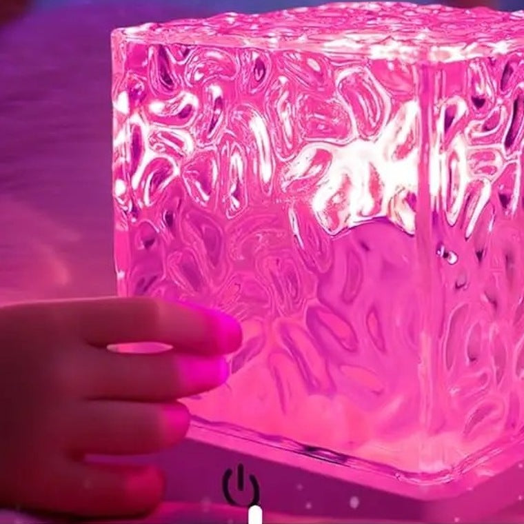 A hand touching the base of the cube lamp lit in bright pink